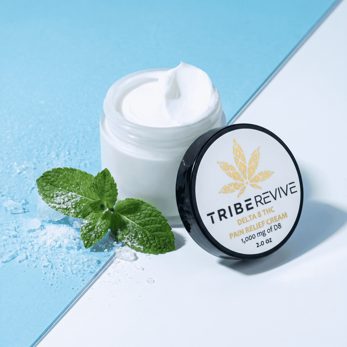 Open jar of TribeRevive Delta 8 THC Pain Relief Cream with fresh mint and crushed ice on a blue and white background, cueing the cooling effect