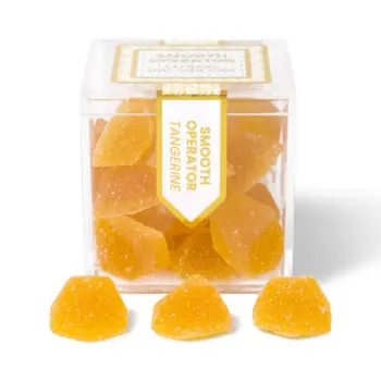 TribeTokes Smooth Operator Tangerine gummies in a clear cube box with three sugar-coated gummies in front on a white background