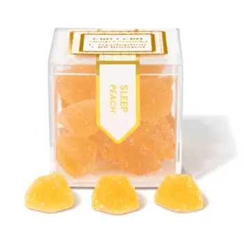 TribeTokes Sleep Peach gummies in a clear cube box with three sugar-coated peach gummies in front on a white background