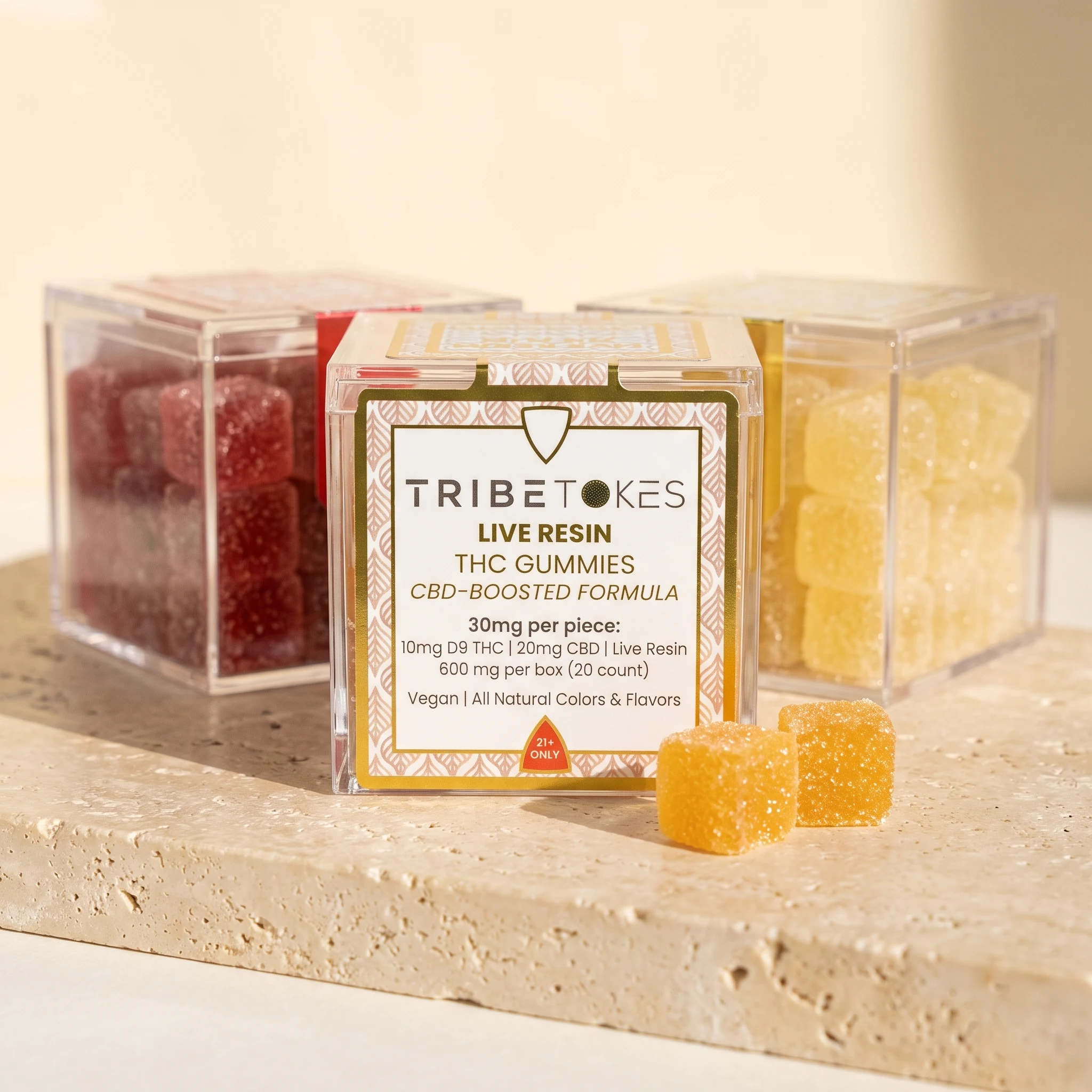 Three flavors of TribeTokes Live Resin THC gummies on a travertine slab, with the Mango box front label showing 10mg Delta 9 THC and 20mg CBD per piece, 600mg per box