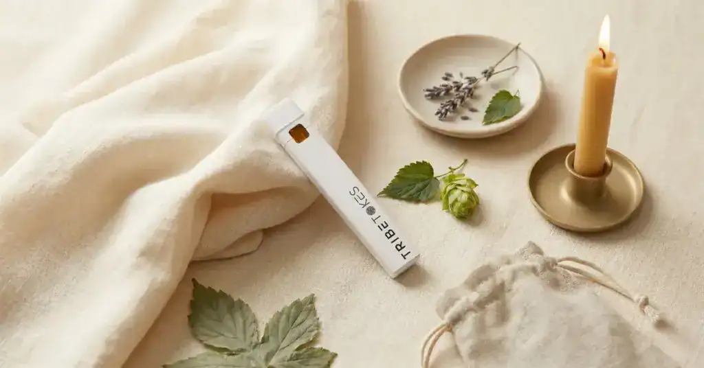 TribeTokes indica disposable vape pen on cream linen with dried lavender, fresh cannabis leaves, and a lit beeswax candle — nighttime sleep ritual