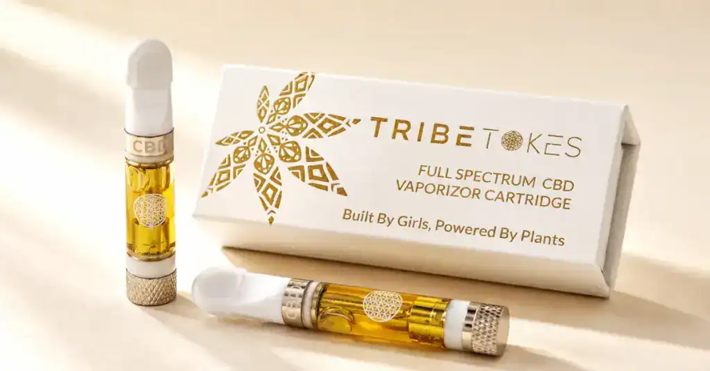 Two TribeTokes vape cartridges with amber live resin oil visible through the glass chamber beside a white product box on a cream background representing dab cart quality and concentrate extraction guide