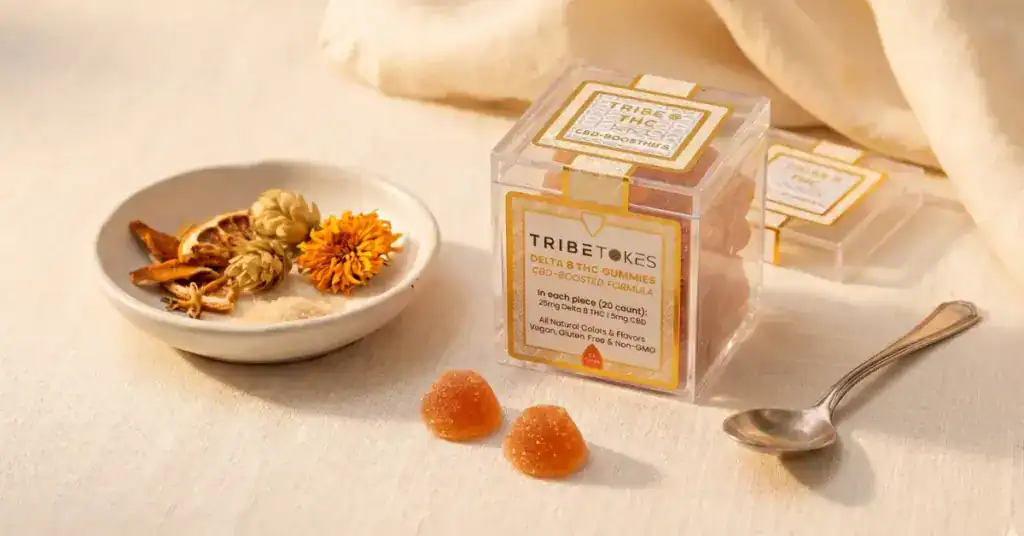TribeTokes Delta 8 THC CBD-boosted gummies in clear acrylic jar with loose strawberry gummies on warm cream linen surface — Delta 8 complete guide