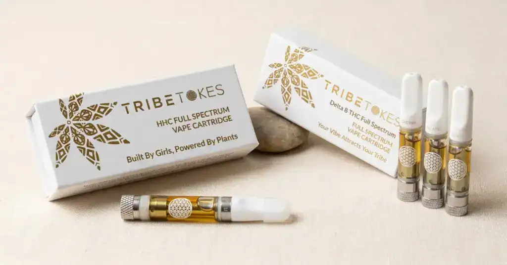 TribeTokes HHC Full Spectrum vape cartridge and Delta-8 Full Spectrum vape cartridge side by side on cream surface — cannabinoid potency comparison