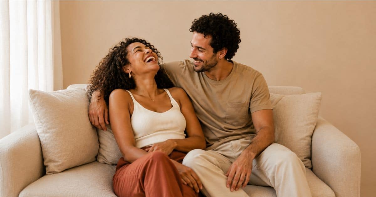 Man and woman laughing together on a cream couch in natural light, representing cannabis and sexual wellness