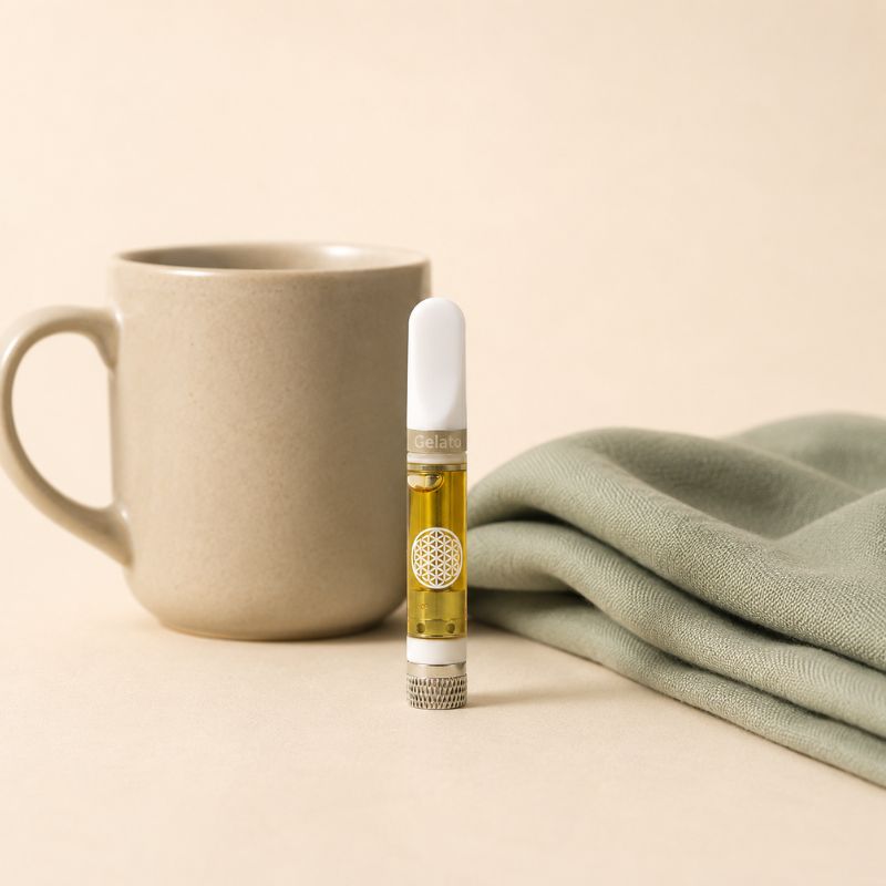 TribeTokes CBD vape cartridge standing beside a matte ceramic mug and a folded sage linen napkin on a cream background with soft natural light creating a calm evening wellness scene.