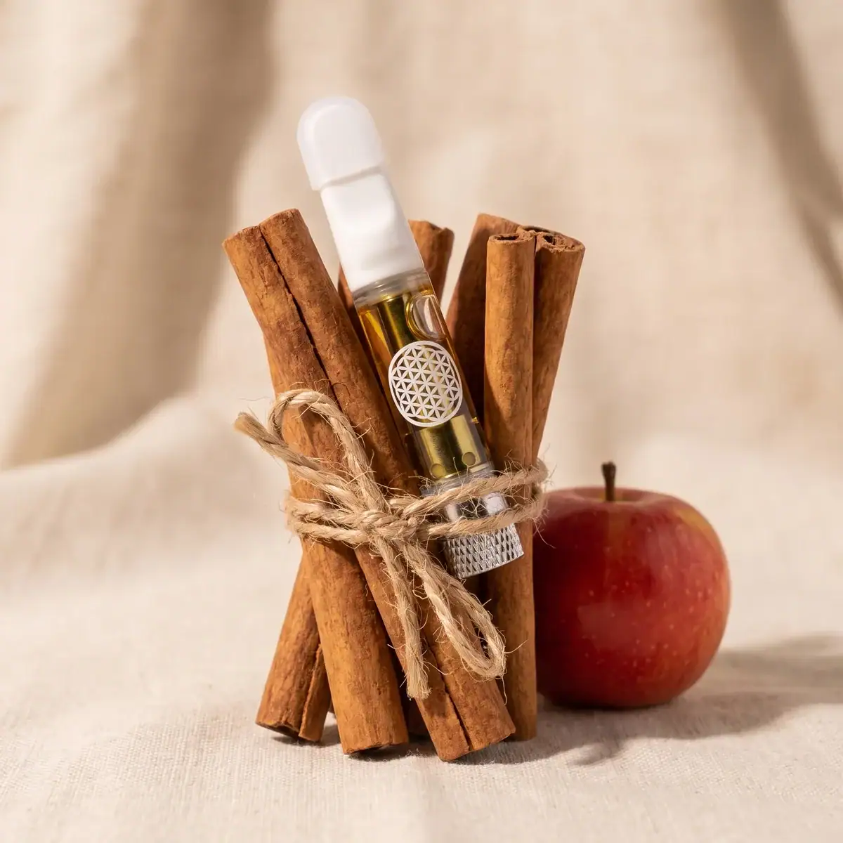 Spiced Apple Cider THCa vape cart tied into a bundle of cinnamon sticks with twine, red apple beside it