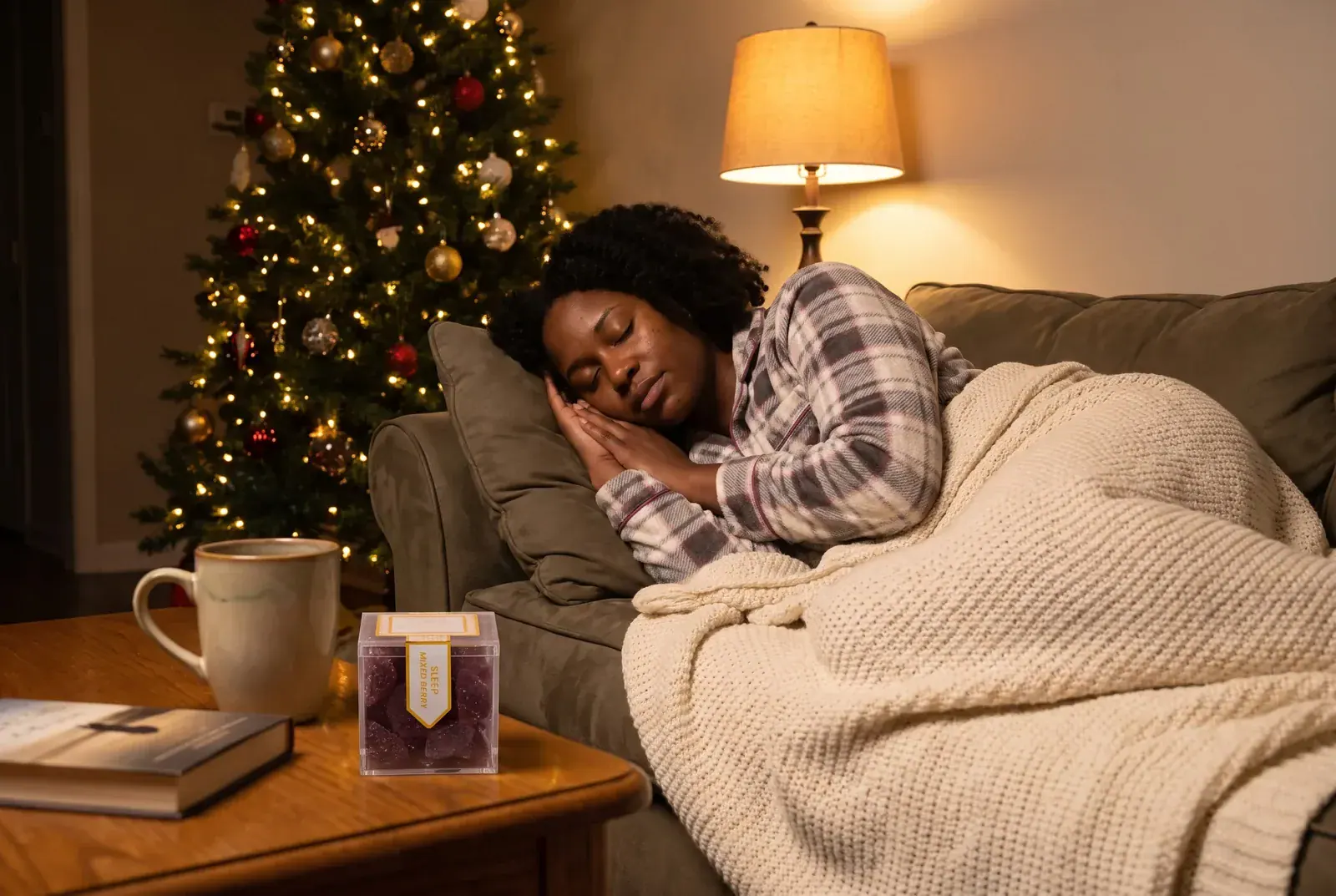 Woman napping under a knit blanket by a Christmas tree with TribeTokes Mixed Berry gummies on the coffee table