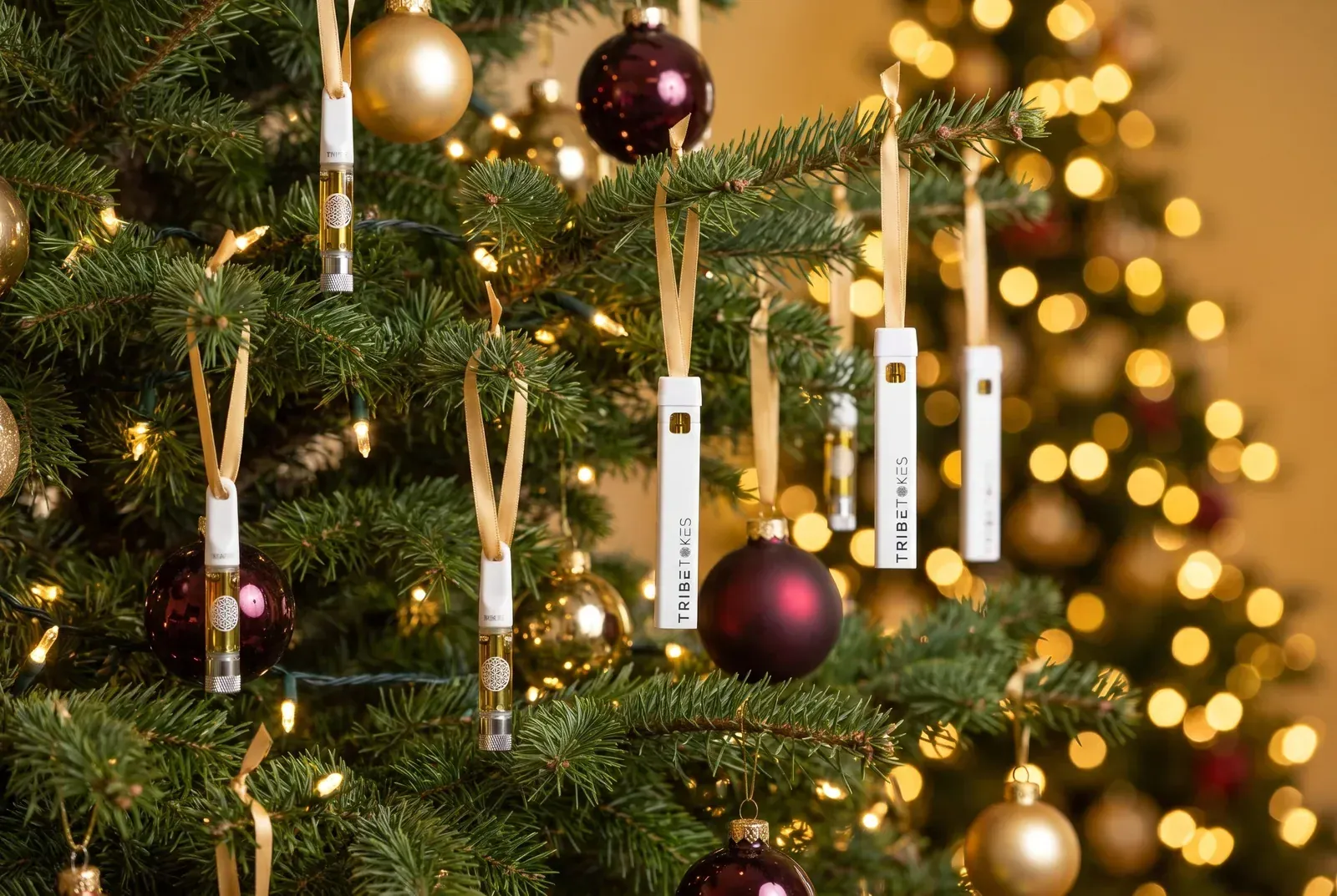 TribeTokes THCa vape cartridges and disposable pens hung on gold ribbons as ornaments on a lit Christmas tree